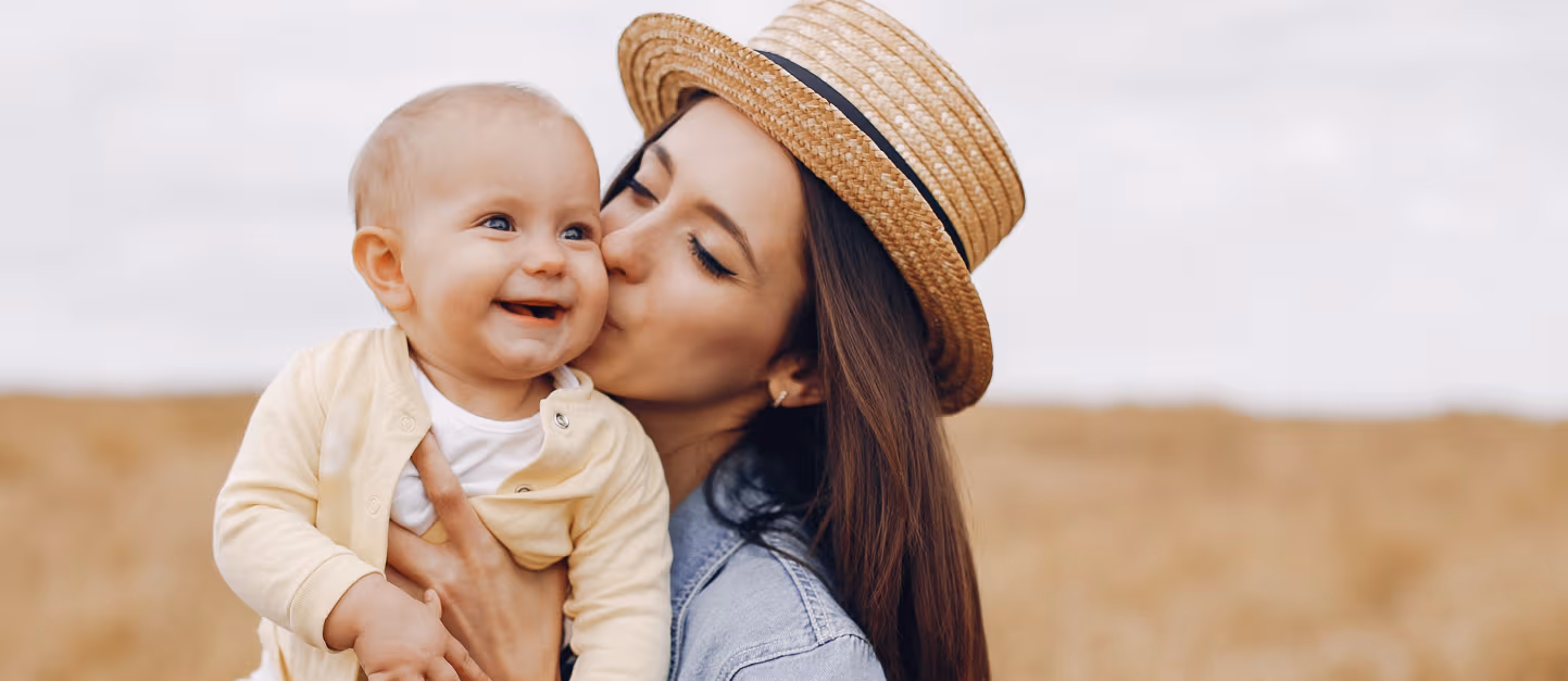 Mom in a straw hat kissing her baby in a field